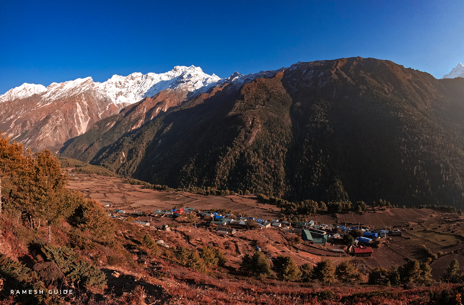 Chhekampar village in Tsum Valley surrounded by traditional stone houses, green hills and Himalayan mountains.